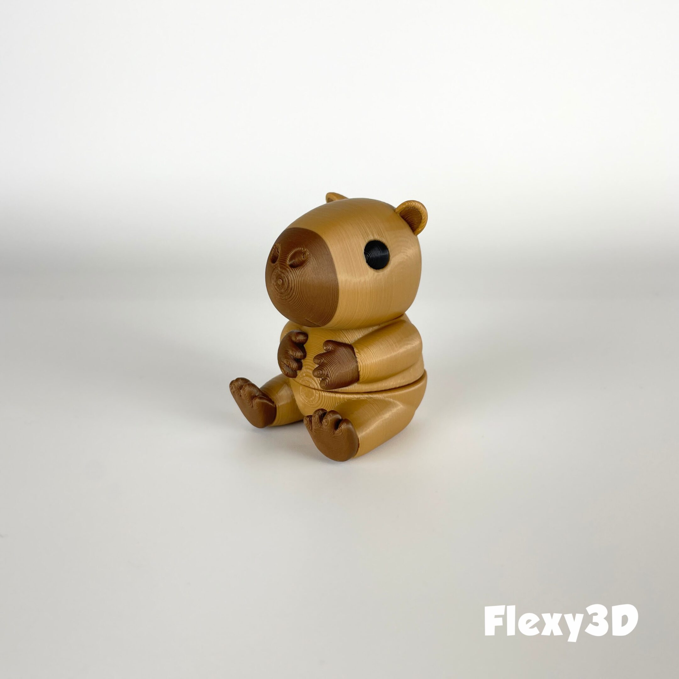 A small, golden teddy bear figurine sitting on a white surface.