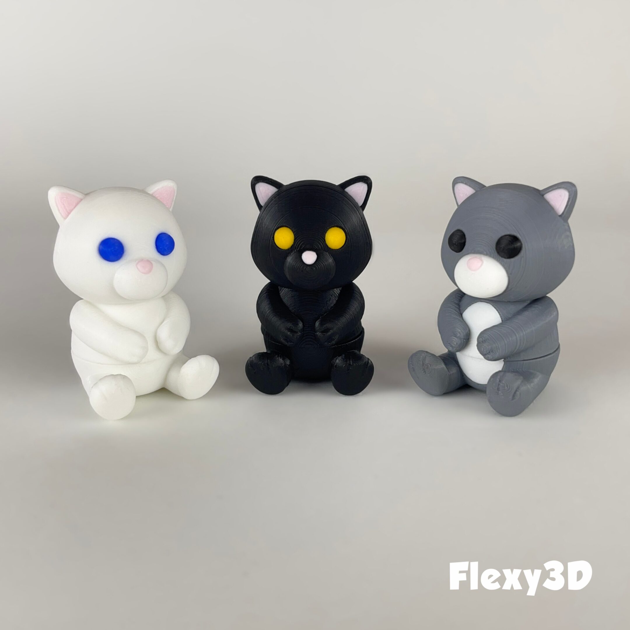 Three small cat figurines in white, black, and gray colors.