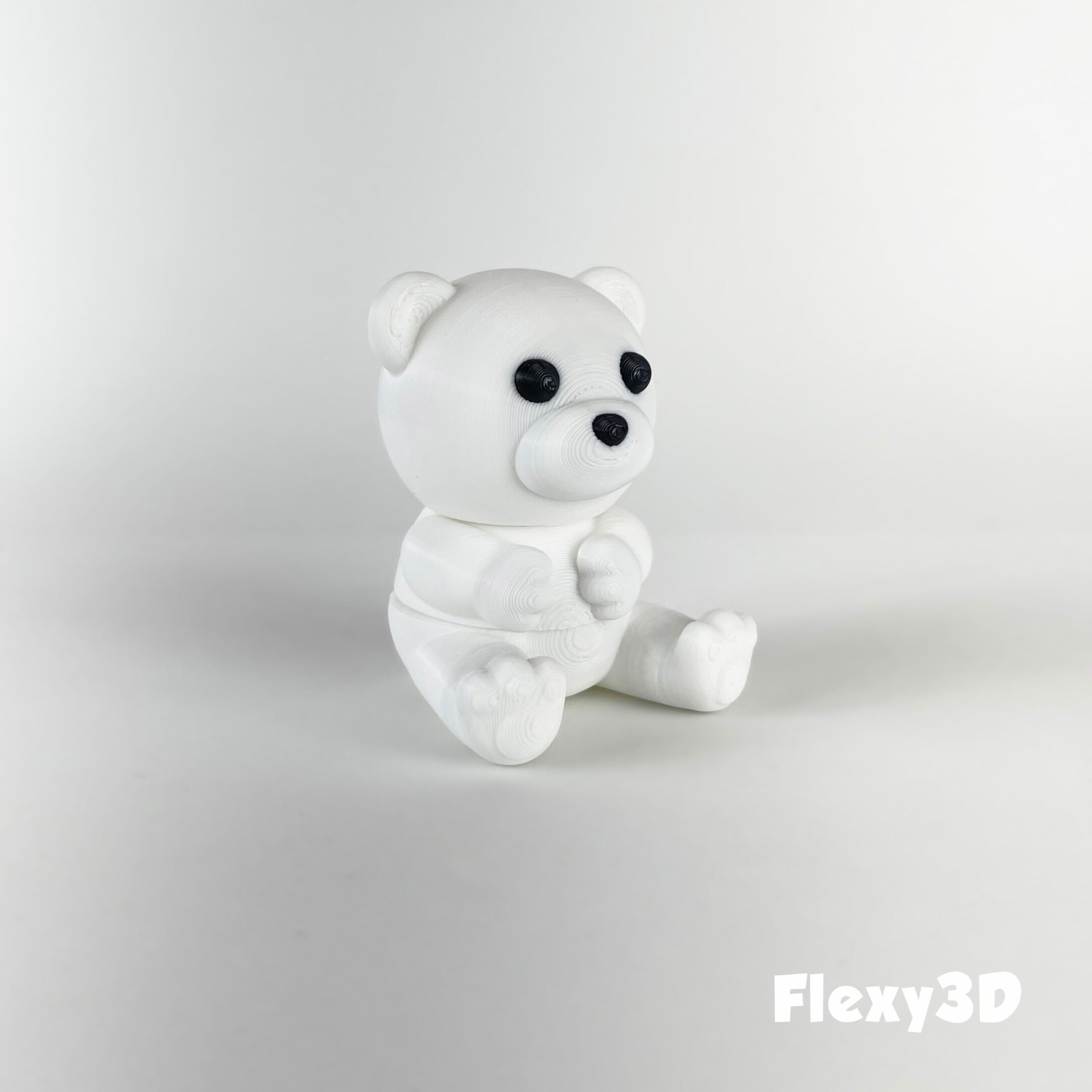 A small white teddy bear figurine sitting on a plain white surface.