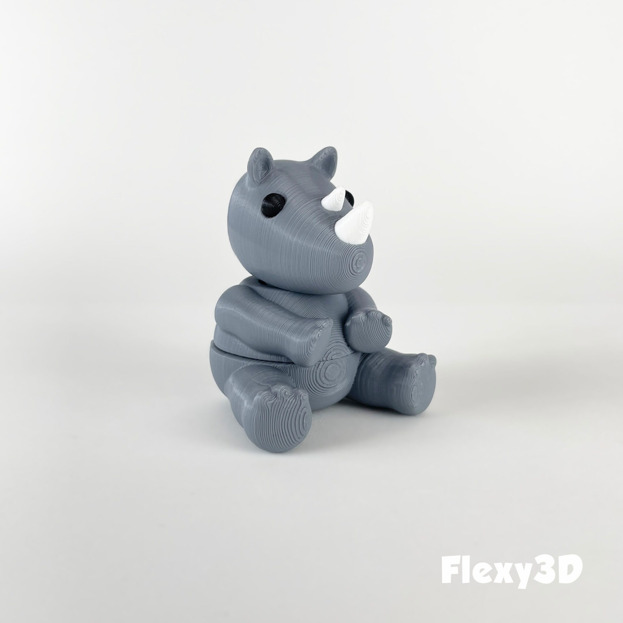 A small, gray, stylized rhinoceros figurine sitting on a white surface.