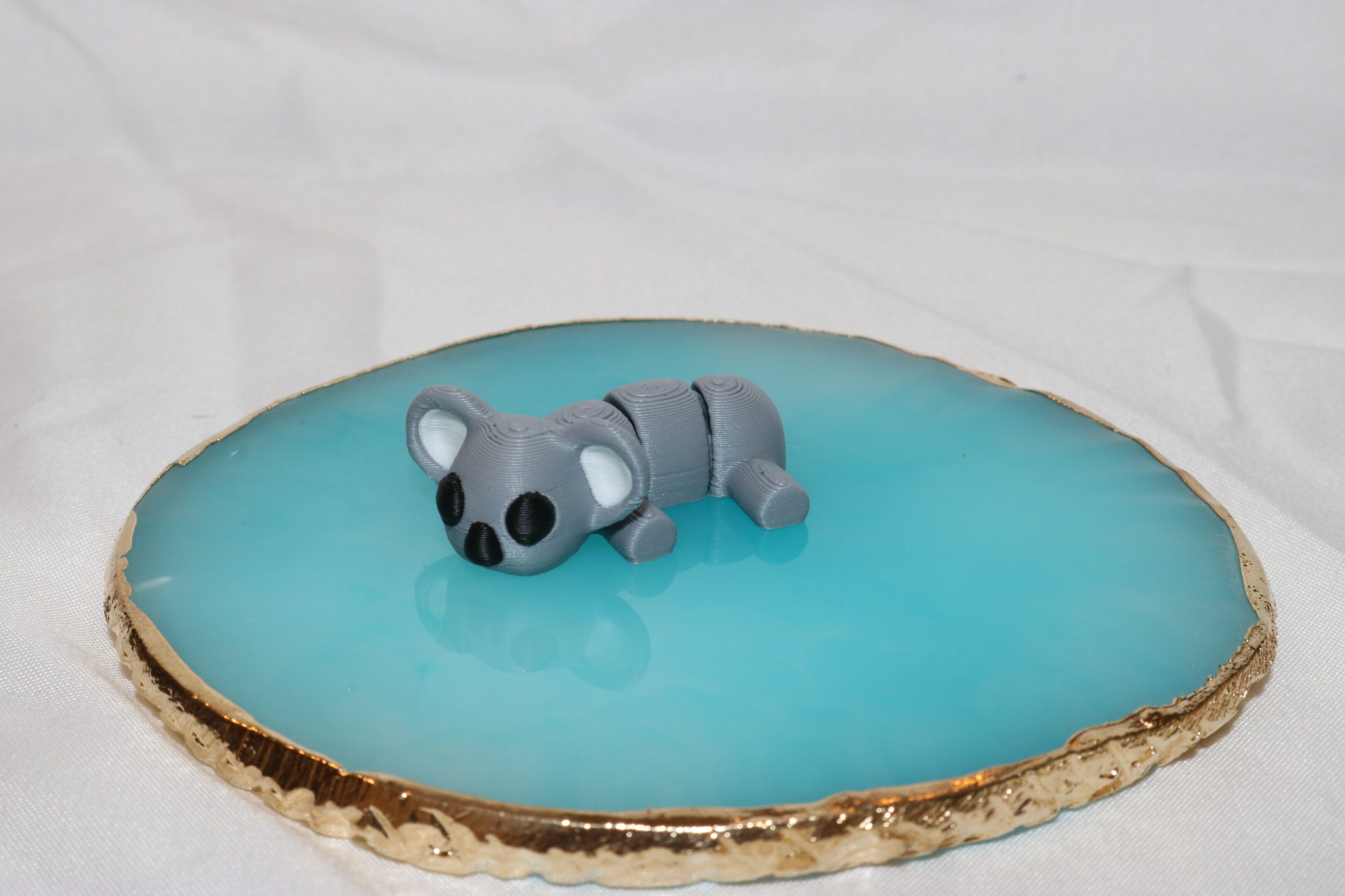 A small, gray, clay koala on a blue surface.