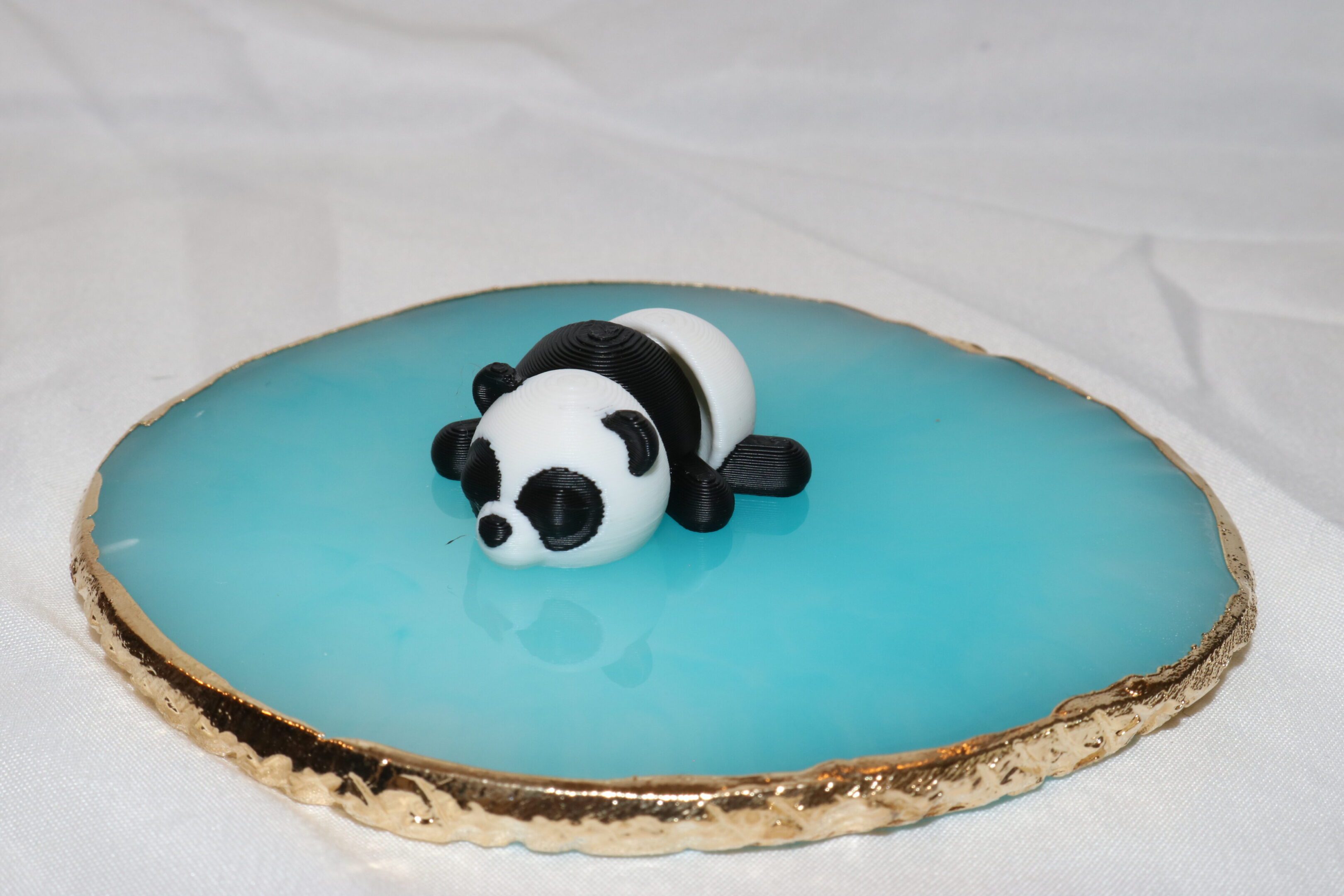 A small panda figurine rests on a glossy blue surface with a gold edge.