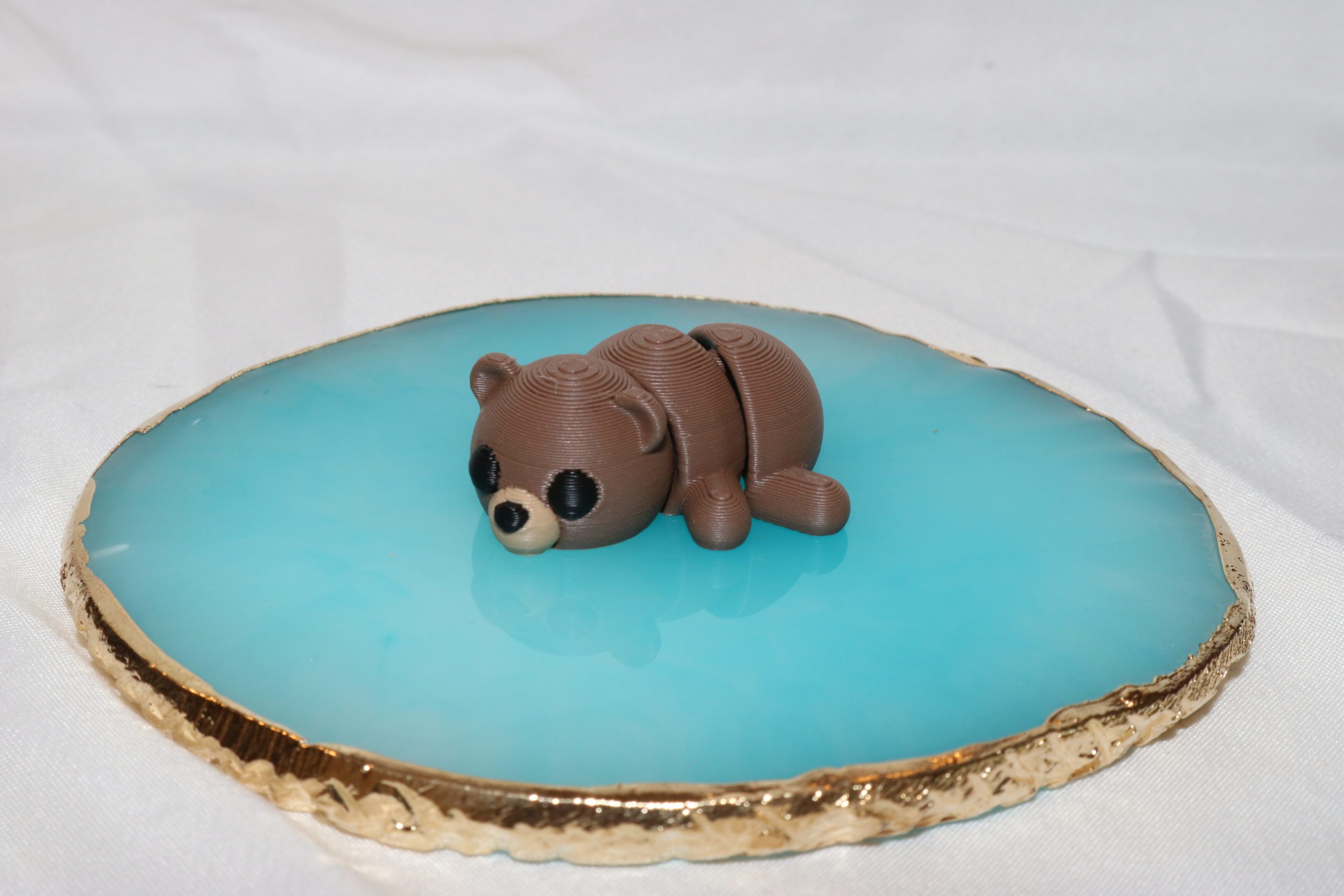 A small, brown bear figurine resting on a blue, shiny surface.