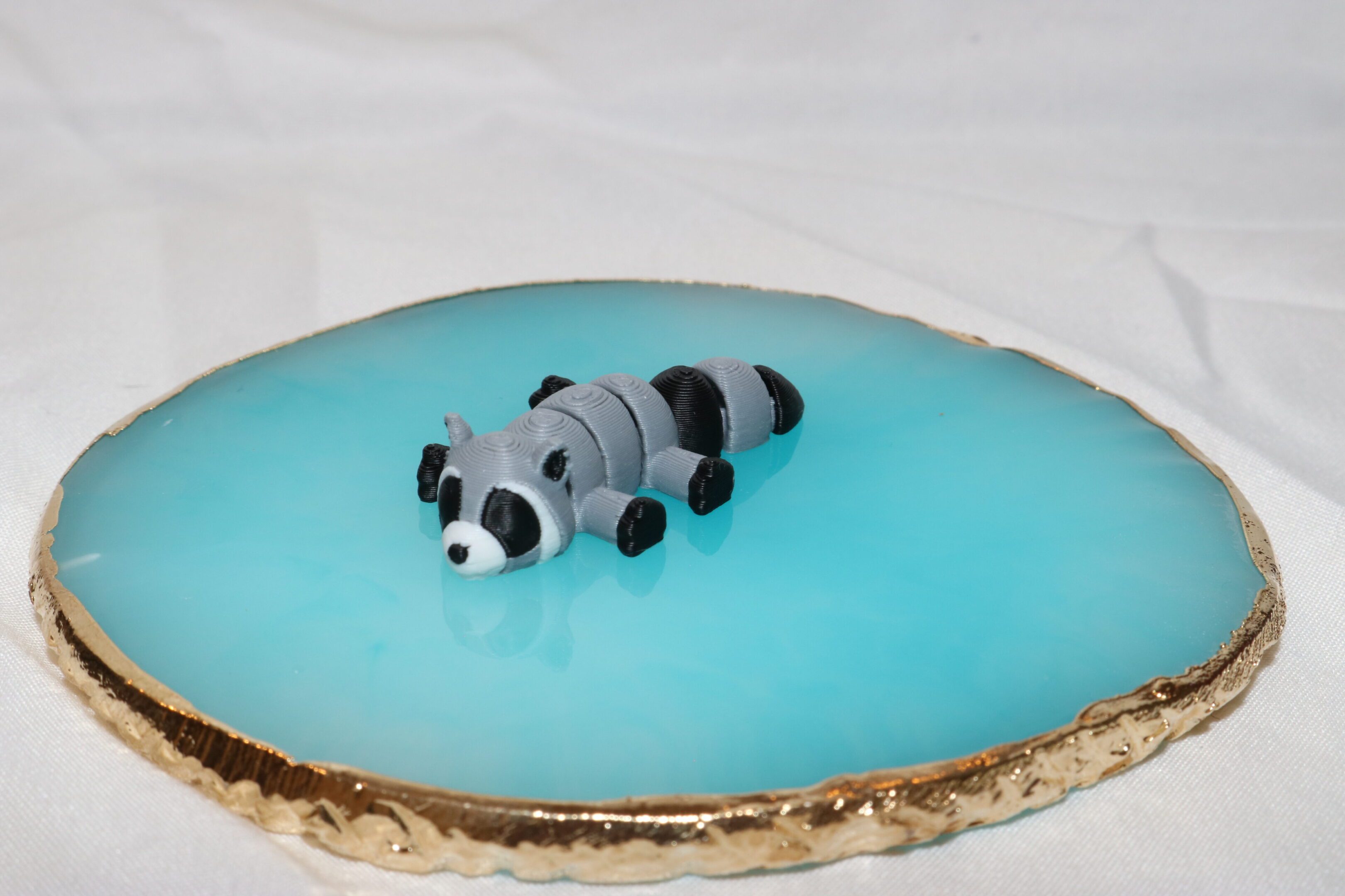 A cute raccoon figurine on a blue cake with a golden base.