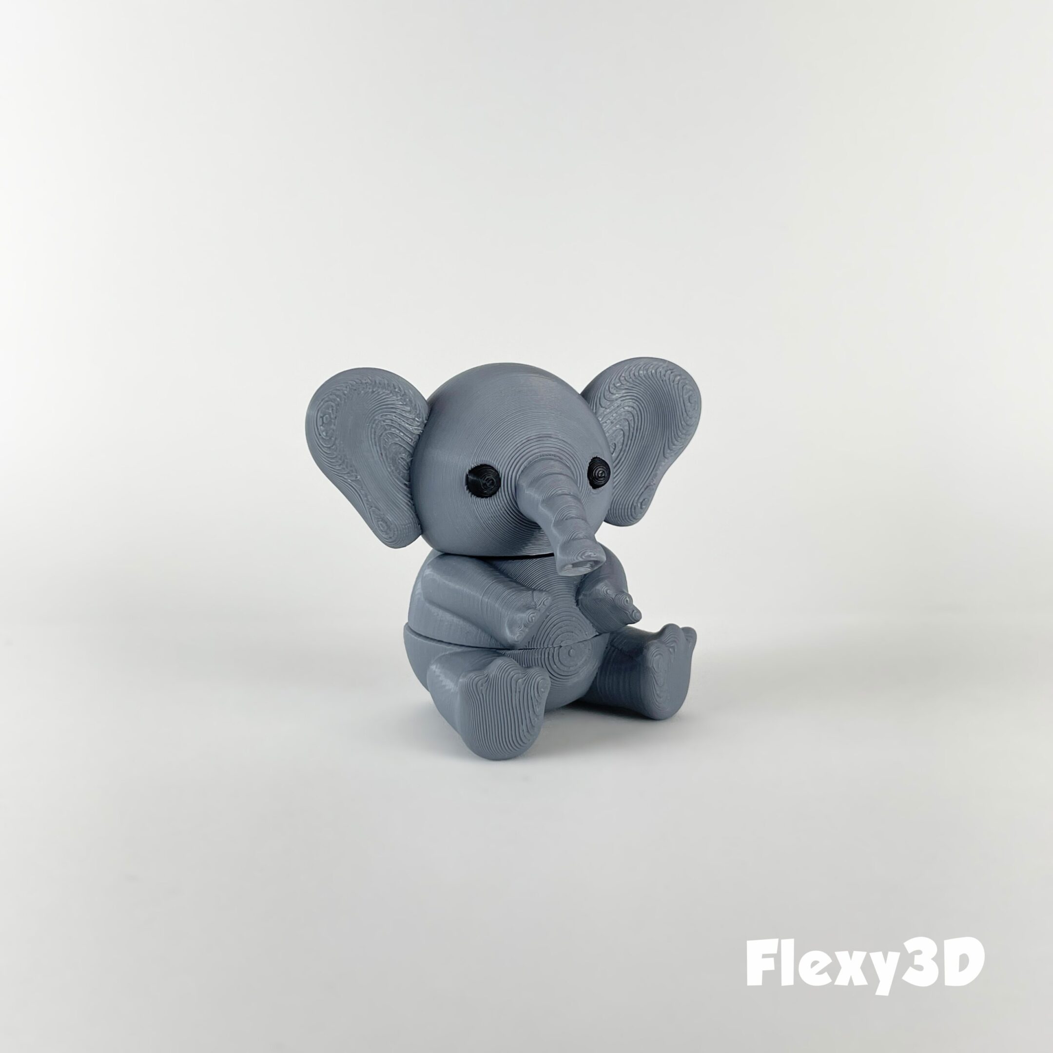 A cute gray elephant figurine sitting on a white surface.