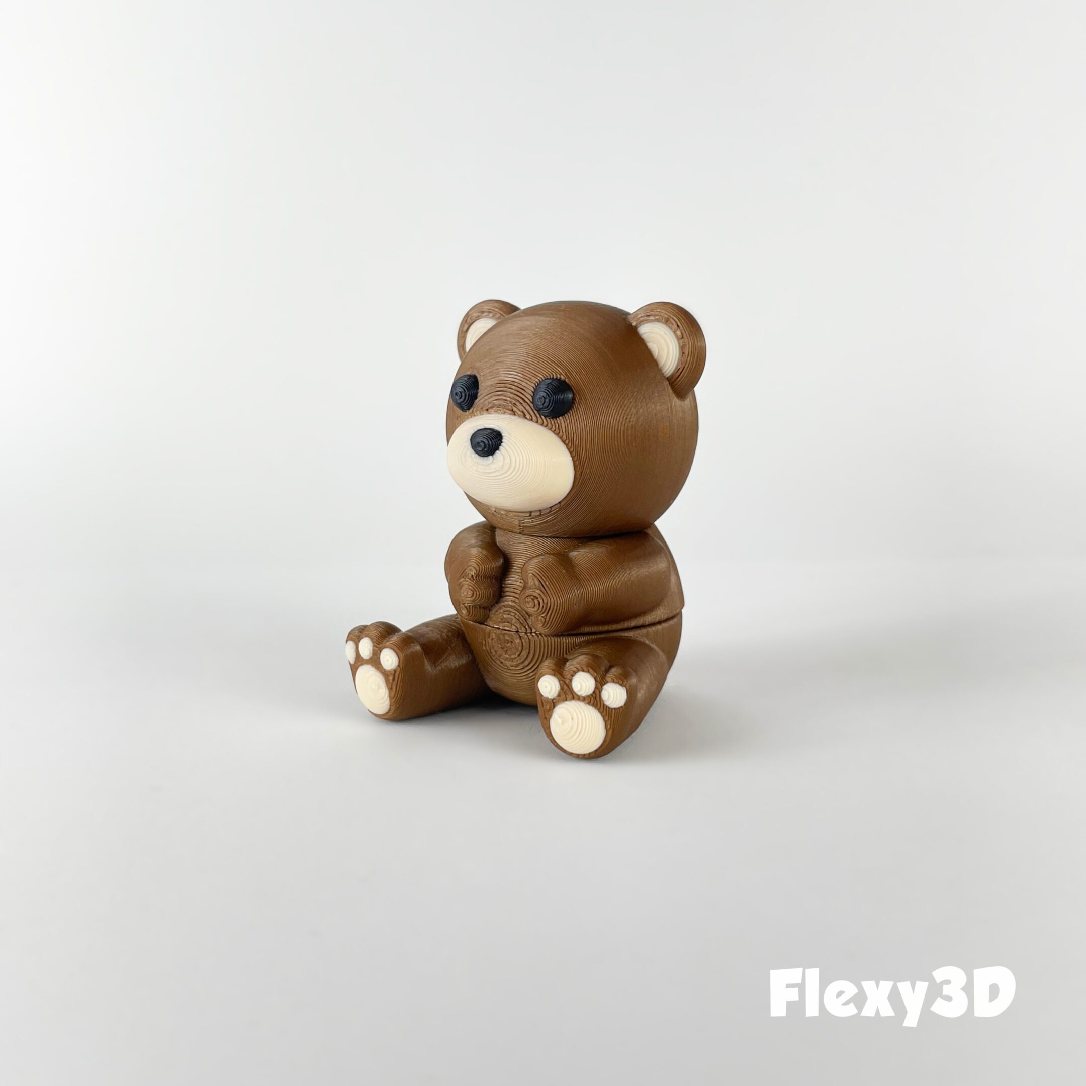 A small, brown teddy bear figurine sitting on a white surface.