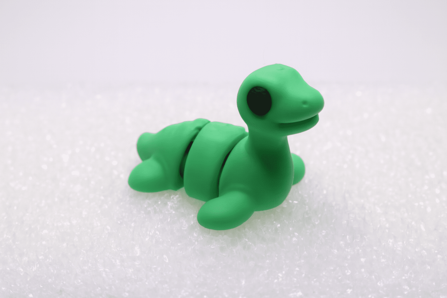 A small, green, segmented turtle figurine on a white surface.