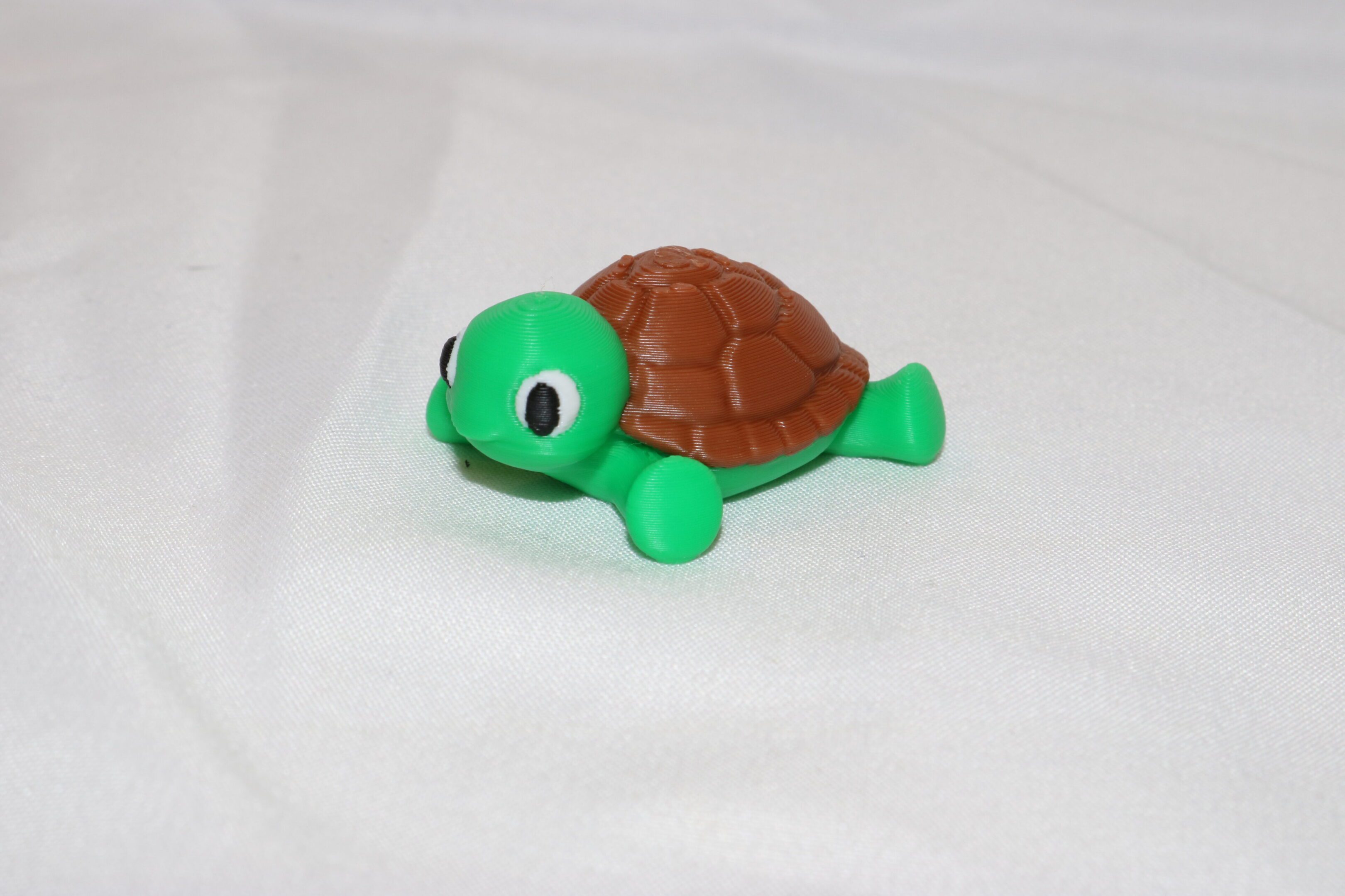 A small green toy turtle with a brown shell on a white surface.