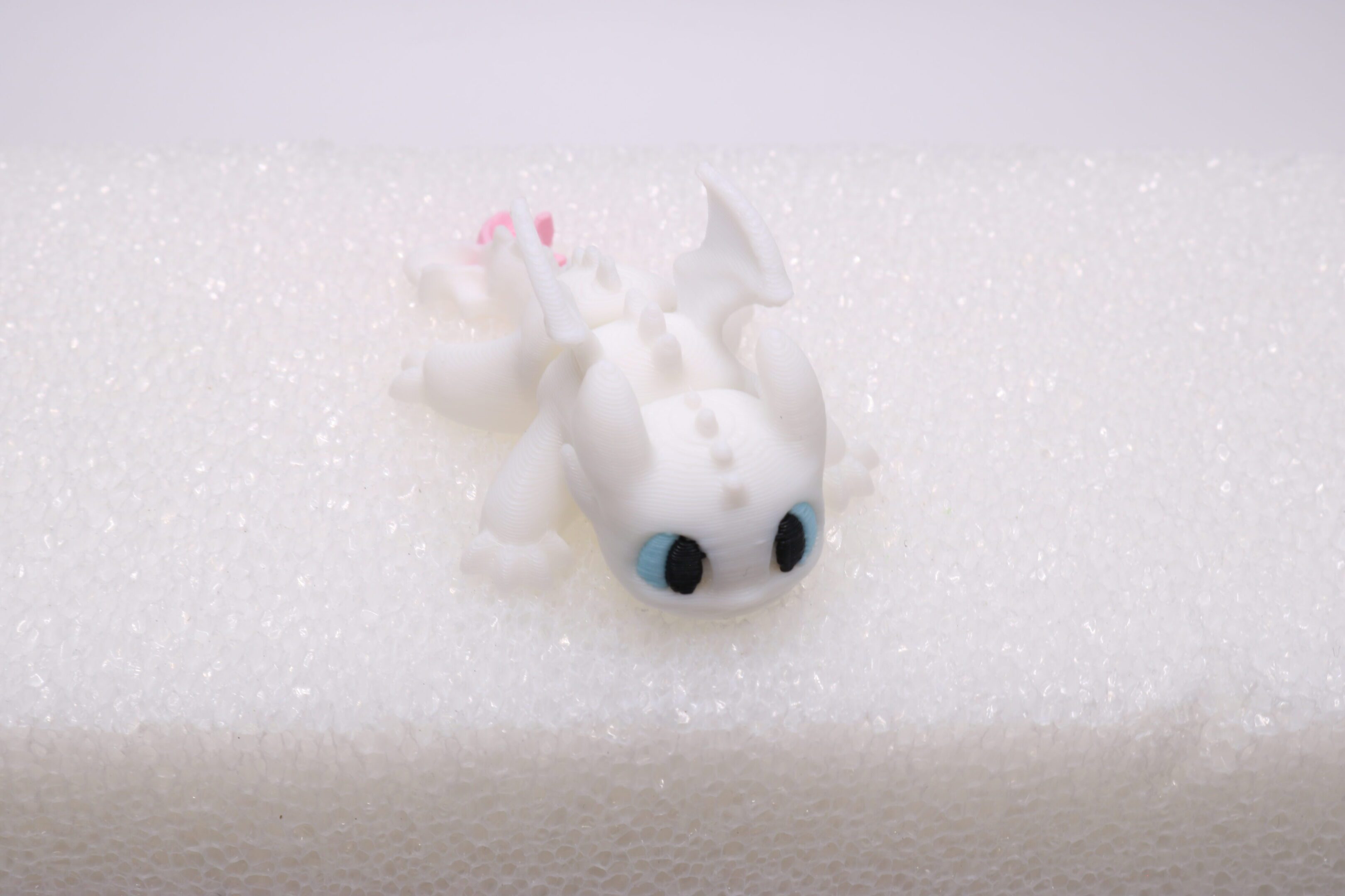 A small, white dragon figurine with blue eyes on a white surface.