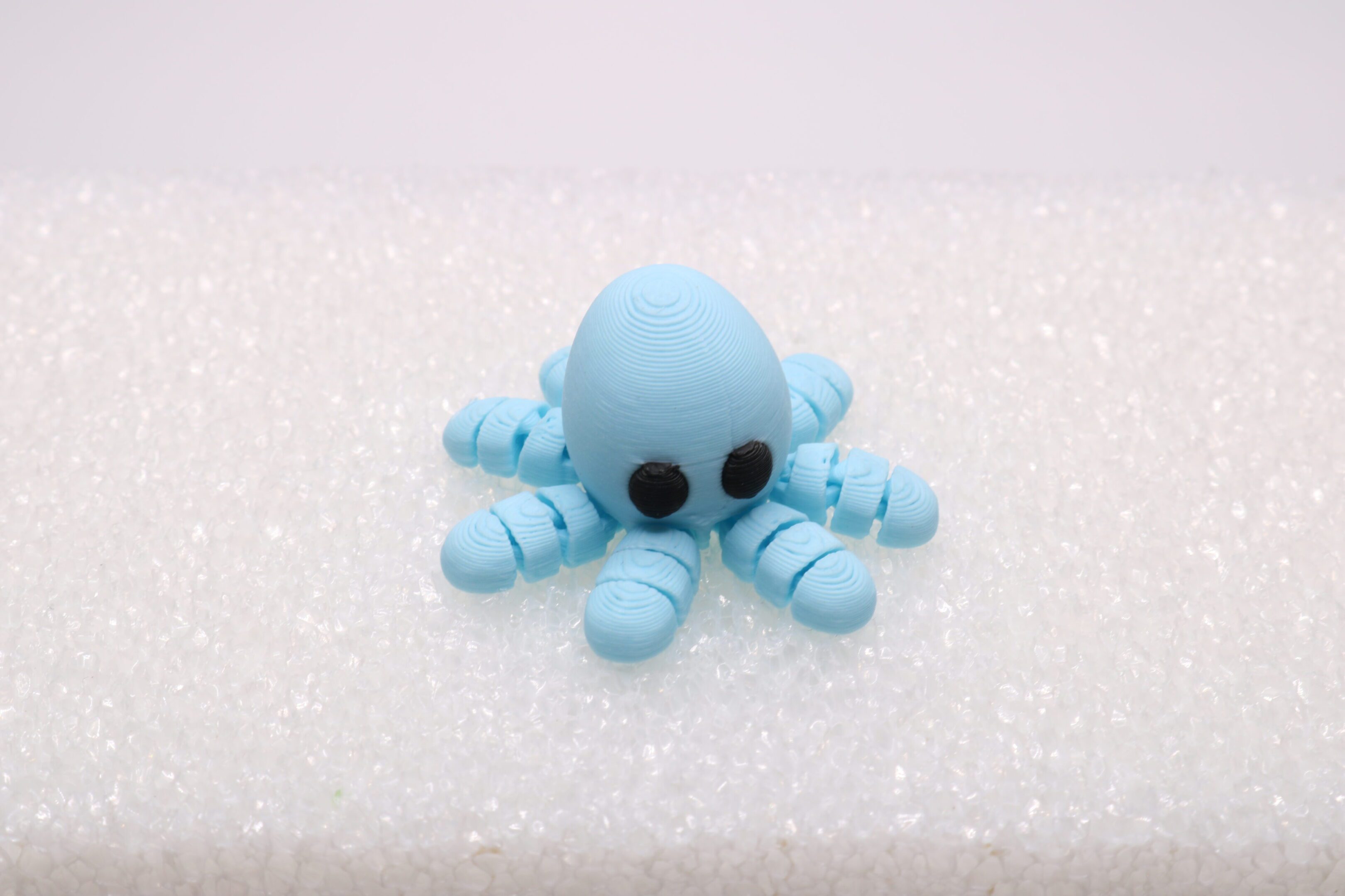 A cute blue octopus figurine with black eyes on a white surface.