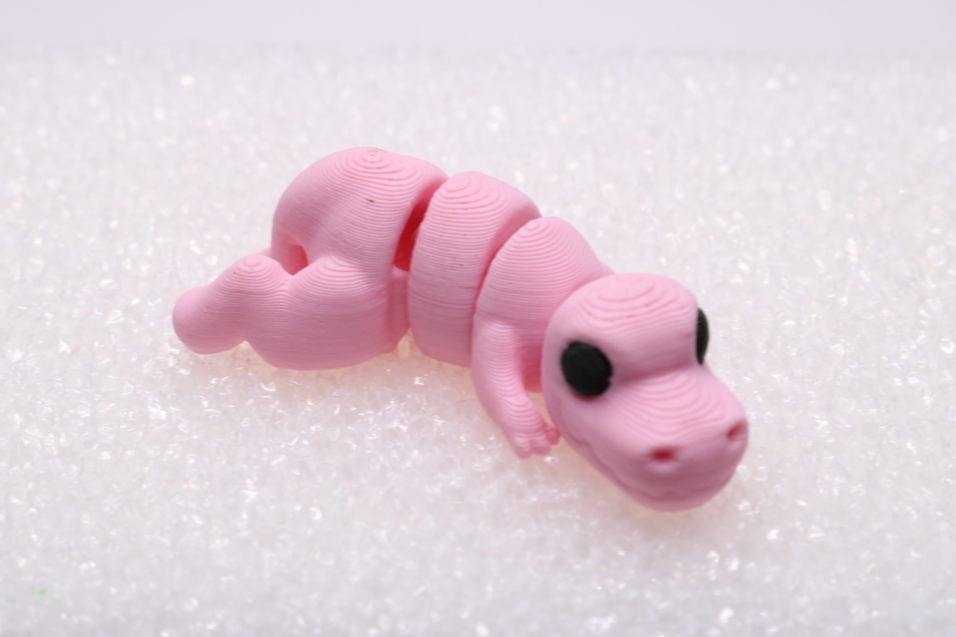 A small pink alligator clay figure with black eyes on a white surface.