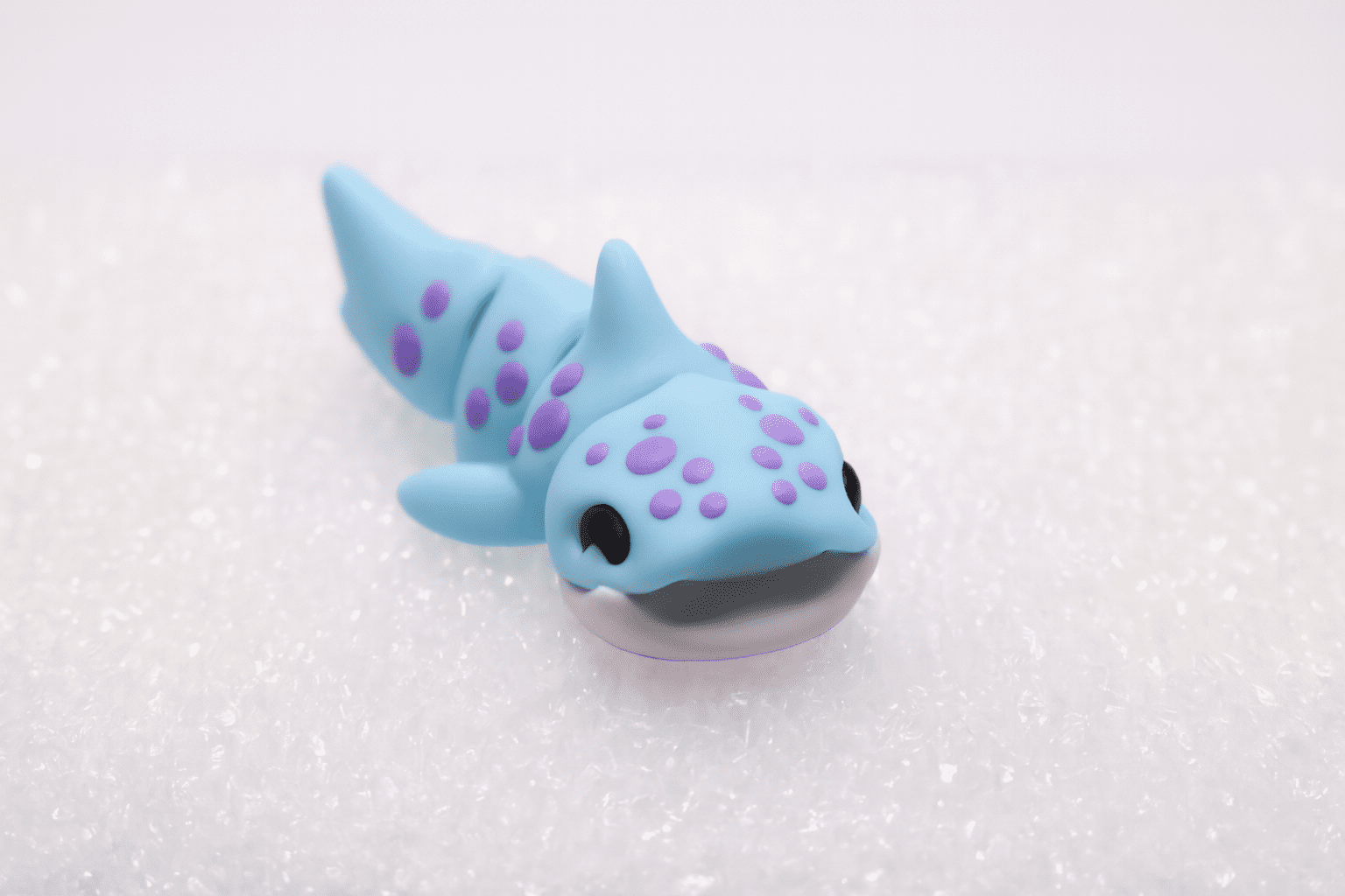 A small blue shark figurine with purple spots on a white surface.