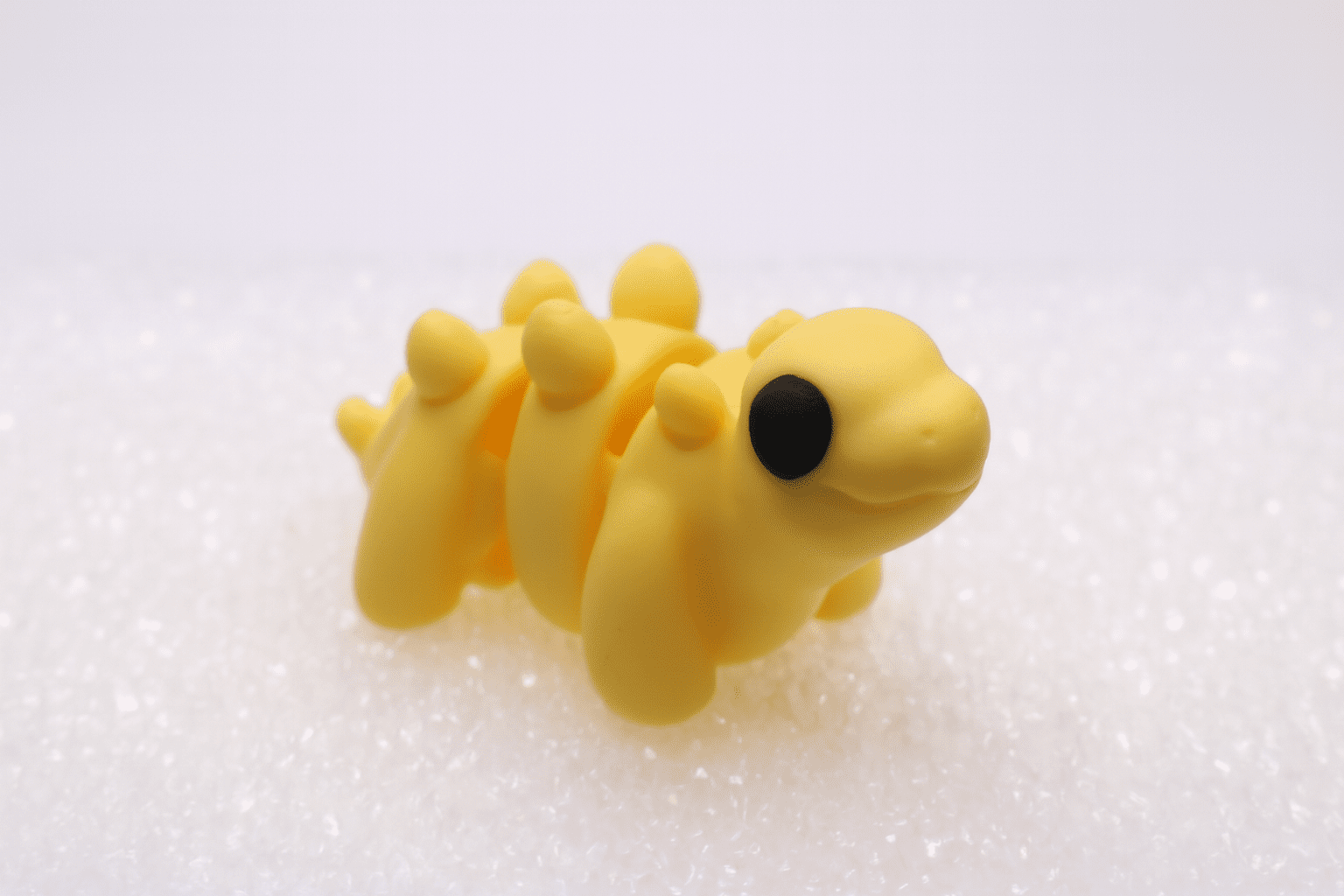 Close-up of a yellow, segmented caterpillar with a black head on a white surface.