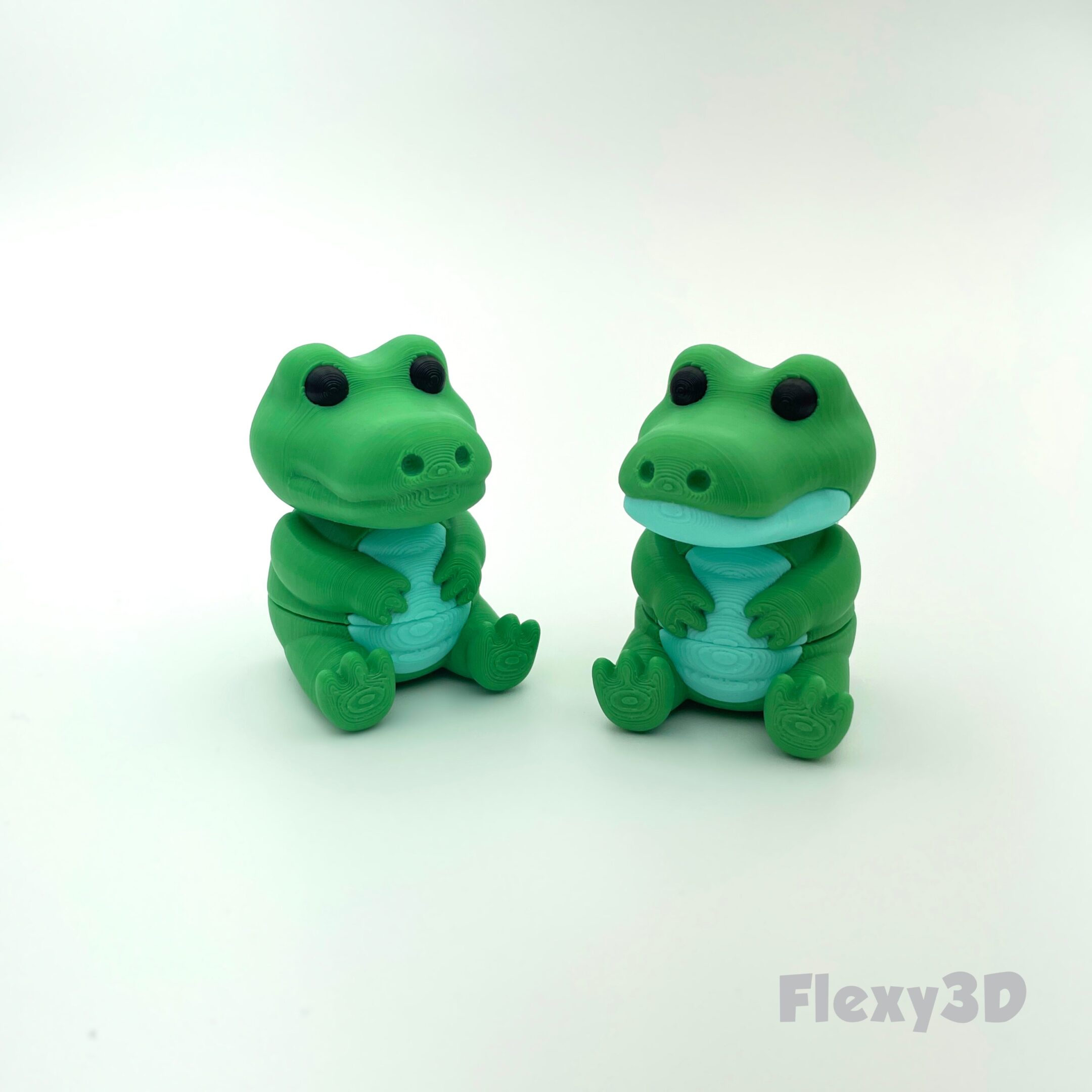 Two small green frog figurines standing on a white surface.